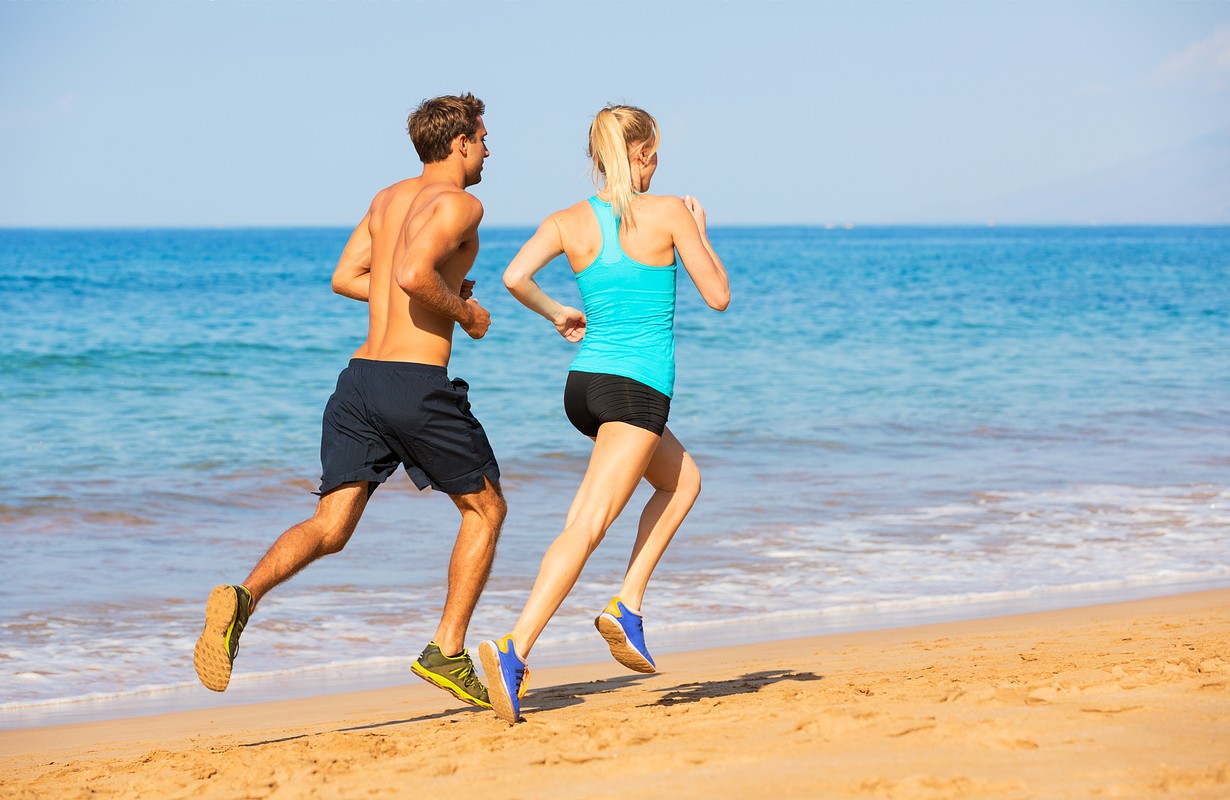 Sport runners jogging on beach working out smiling happy. 