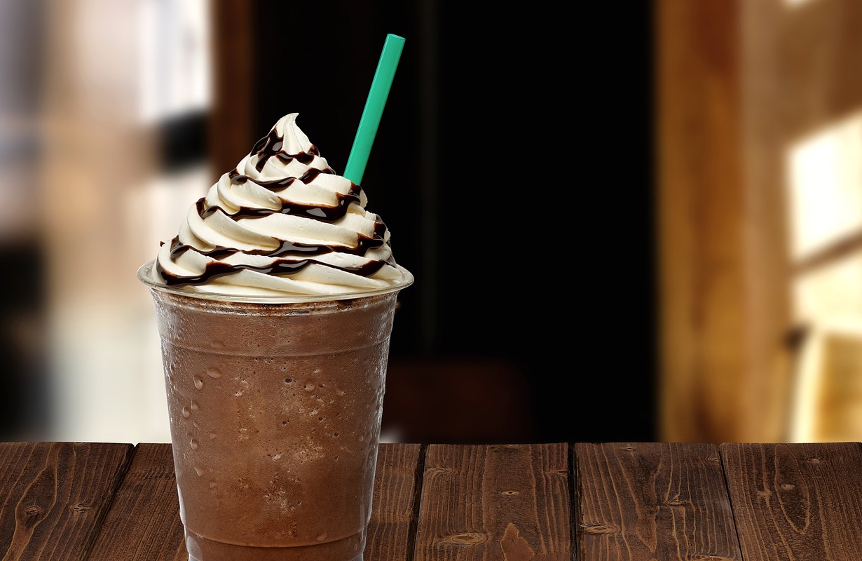 Frappuccino in takeaway or to go cup on wooden table at cafe.