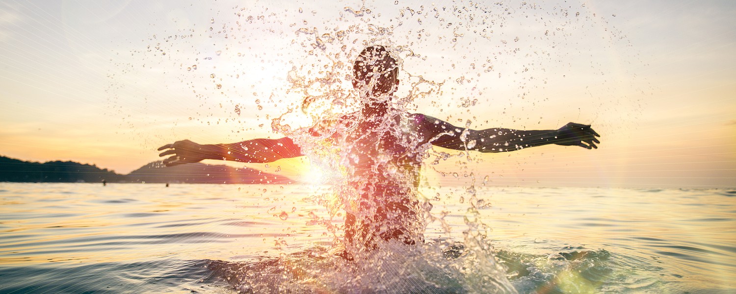 man jumping out of the water in the rays of sunshine