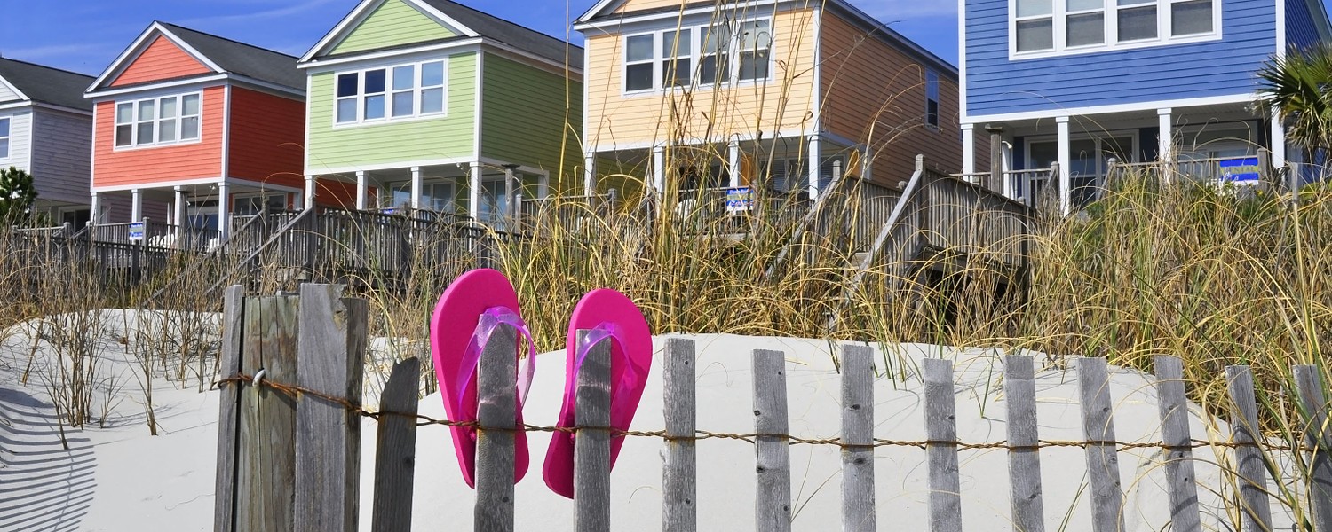 Row of beach rentals on a summer day, pink flip flops on beach fence